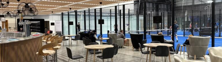 The Padel Hub Crawley Image 1 showing indoor padel courts with players in action and a stylish bar area in the foreground, highlighting the club’s dynamic mix of sport and social space in Crawley, West Sussex.