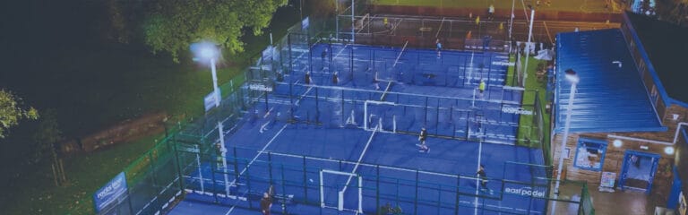 Rocks Lane Tennis Club Chiswick aerial view showing outdoor padel courts with floodlights on, highlighting the club’s well-equipped facilities for evening play in West London.