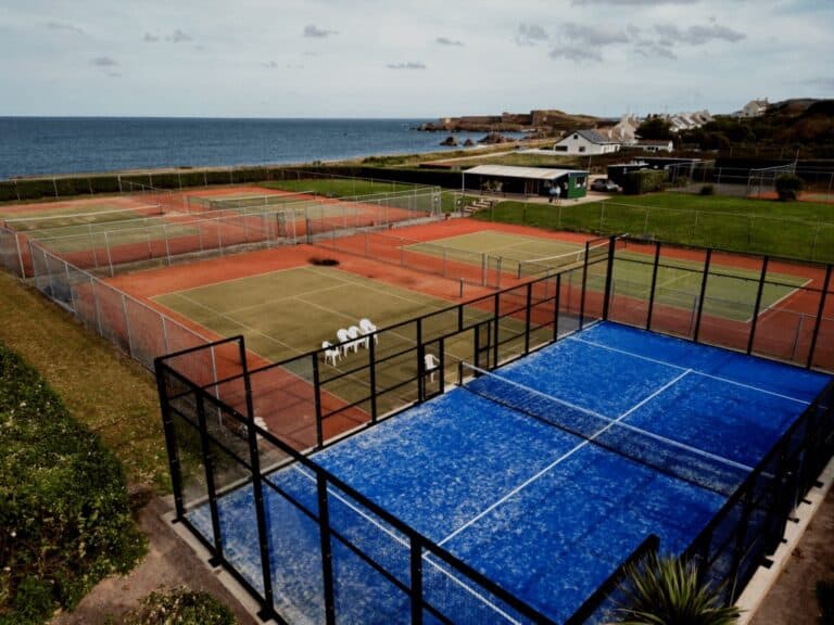 Empty tennis and padel courts at Alderney Tennis Club, situated next to the sea with scenic coastal views in the background, under an open sky.